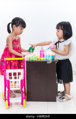 Asiatische chinesische kleine Schwestern so zu tun als Kassierer und Kunden mit Trolley Spielzeug in isolierten weißen Hintergrund. Stockfoto