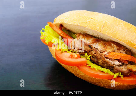 Sandwich: Fleisch Brötchen mit Gemüse in einem Brötchen mit Tomate und Salatblätter auf dem schwarzen Hintergrund. Stockfoto