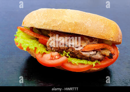 Sandwich: Fleisch Brötchen mit Gemüse in einem Brötchen mit Tomate und Salatblätter auf dem schwarzen Hintergrund. Stockfoto