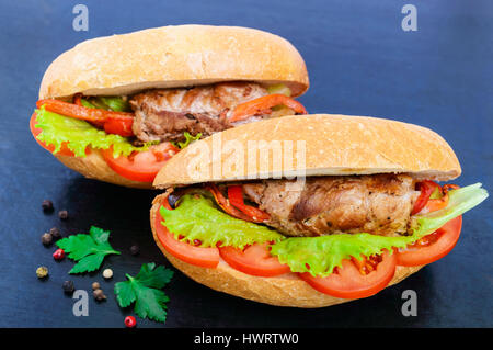 Sandwich: Fleisch Brötchen mit Gemüse in einem Brötchen mit Tomate und Salatblätter auf dem schwarzen Hintergrund. Stockfoto
