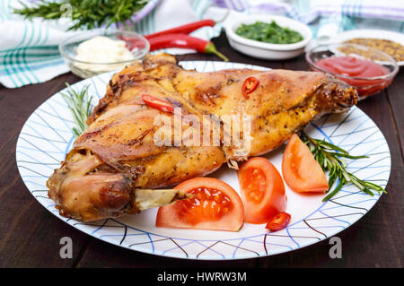 Gebackenes Kaninchen Beine auf einen Teller und verschiedenen Saucen für Fleisch auf einem dunklen Hintergrund aus Holz. Stockfoto