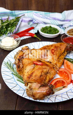 Gebackenes Kaninchen Beine auf einen Teller und verschiedenen Saucen für Fleisch auf einem dunklen Hintergrund aus Holz. Stockfoto
