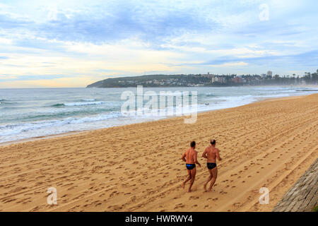 Menschen zwei Männer trainieren beim Laufen und Joggen am Manly Beach in der Morgendämmerung, Sydney, Australien Stockfoto