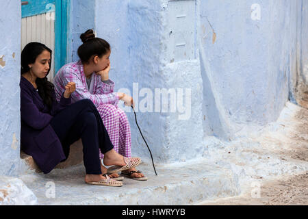 Chefchaouen, Marokko.  Zwei junge Frauen sitzen auf einer Türschwelle. Stockfoto