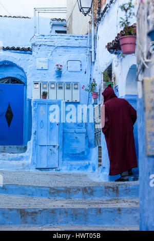 Chefchaouen, Marokko.  Mann im Eingangsbereich zu seinem Haus.  Nachbarschaft Stromzähler auf Wand vor. Stockfoto