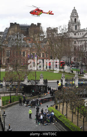 Ein Air Ambulance landet wie Notfalldienste zu besuchen, ein Mann (oben) und ein Polizist (unten) außerhalb des Palace of Westminster, London, nachdem ein Polizist wurde erstochen und seine scheinbare Angreifer von Offizieren in einem großen Sicherheitsvorfall beschossen die Houses of Parliament. Stockfoto