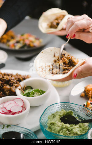 Hand der Frau bereitet Taco mit Freund am Esstisch sitzend beschnitten Stockfoto