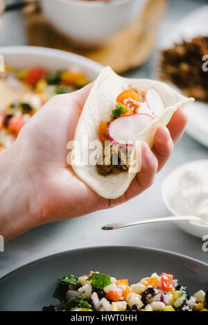 Abgeschnitten von Menschenhand hält Taco am Esstisch Stockfoto