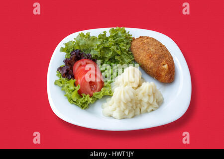 Kartoffelpüree mit einem Schnitzel, Gemüse, Tomaten und grünen Erbsen auf einer roten Tischdecke Stockfoto