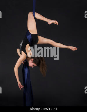 Die junge, lächelnde Frau macht Übungen auf den Leinwänden. Studioaufnahme der Performance auf dunklem Hintergrund. Stockfoto