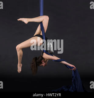 Die junge, lächelnde Frau macht Übungen auf den Leinwänden. Studioaufnahme der Performance auf dunklem Hintergrund. Stockfoto