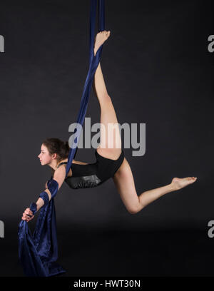 Die junge, lächelnde Frau macht Übungen auf den Leinwänden. Studioaufnahme der Performance auf dunklem Hintergrund. Stockfoto