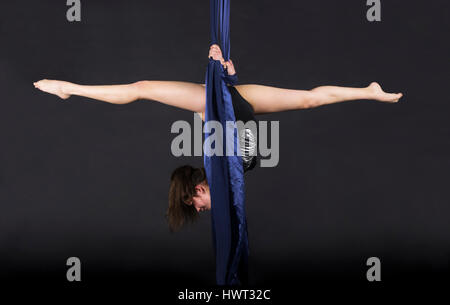 Die junge, lächelnde Frau macht Übungen auf den Leinwänden. Studioaufnahme der Performance auf dunklem Hintergrund. Stockfoto
