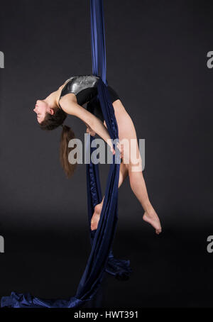 Die junge, lächelnde Frau macht Übungen auf den Leinwänden. Studioaufnahme der Performance auf dunklem Hintergrund. Stockfoto