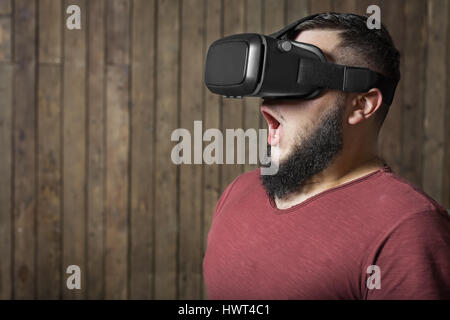 Bärtiger Mann mit virtual-Reality-Brille auf den hölzernen Hintergrund stehend. Konzept der schrecklich, erschreckend, virtuelles Leben Stockfoto