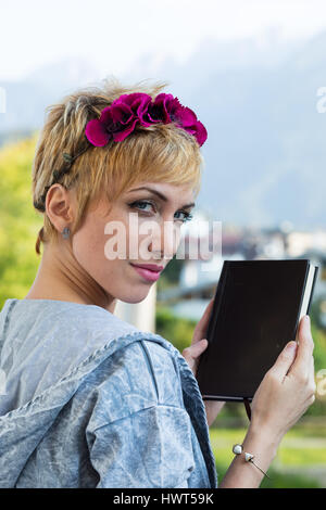 Frau im freien hält ein Buch, sie trägt einen geblümten Stirnband und sie ist im Stil der Kurzhaarschnitt Stockfoto