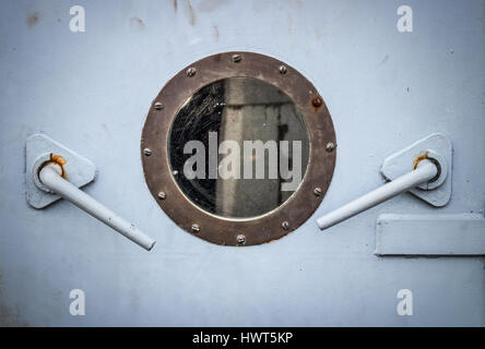 Nahaufnahme von einem Bullauge und zwei Hebel in der grauen Tür eines Schiffes Stockfoto