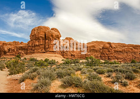 Schöne rote Sandstein Felsformationen werden durch interessante Wolkenformationen im Arches National Park in Utah hervorgehoben.  Grüne Sträucher bieten eine schöne Stockfoto