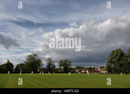 Sonntag Nachmittag Dorf Cricket auf dem Grün in einem Wiltshire Dorf unter einem dramatischen Abend Sommerhimmel. Stockfoto