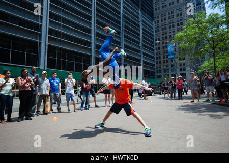 New York City, Usa - 12. Juli 2015: Ein schwarzer Mann, von einer Performance-Gruppe, einen Salto über ein Tourist auf der Straße in Lower Manhattan tut. Stockfoto