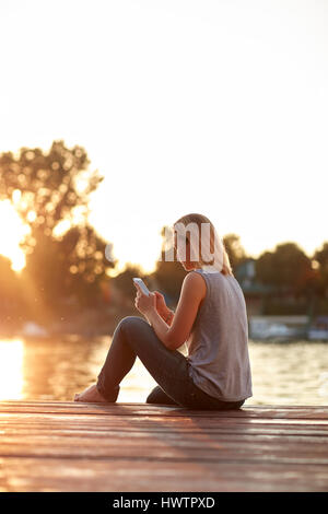 Junge Mädchen mit Handy, genießen im Sonnenuntergang am Fluss Stockfoto