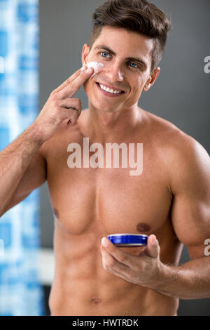 lächelnder Mann Frontspiegel auftragen Kosmetik Creme, Konzept gesunde Hautpflege Stockfoto