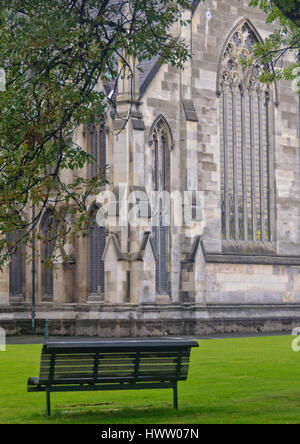 Bank im Garten von der ersten Kirche von Otago und das große gotische Fenster des Querschiffs - Dunedin, Südinsel, Neuseeland Stockfoto