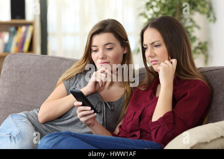 Zwei verärgert Freunde anzeigen auf Linie Inhalt in ein intelligentes Telefon sitzen auf einem Sofa im Wohnzimmer zu Hause Stockfoto