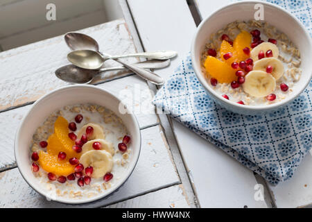 Getränkte Haferflocken in Milch mit Banane, Orange und Granatapfel Samen Stockfoto