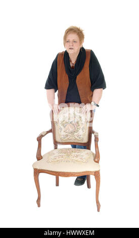 Eine ältere Frau in den Siebzigern stehen hinter einem alten Sessel, ernst, für weißen Hintergrund isoliert. Stockfoto
