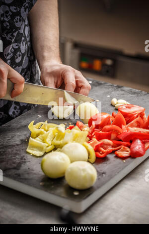 Koch ist auf eine schwarze Schneidebrett in der Restaurantküche Gemüse schneiden. Stockfoto