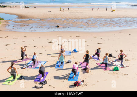 Frauen üben Yoga am Strand von Tynemouth an einem sonnigen Morgen. Im Hintergrund, in der Nähe der Küste sind andere Menschen auszuüben. Stockfoto