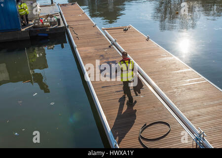 Ein Arbeiter zu Fuß über einen Steg auf dem Wasser schwimmt, seine Kollegen zu Beginn des Arbeitstages beizutreten. Stockfoto