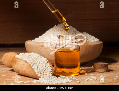 Frische Sesamöl in einer Glasflasche und Samen in hölzerne Schüssel und Löffel auf hölzernen Hintergrund Stockfoto