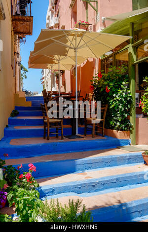 Terrasse mit Stühlen, Tischen und Sonnenschirmen auf einer Treppe in einer engen Straße auf der Insel Kreta-Griechenland Stockfoto