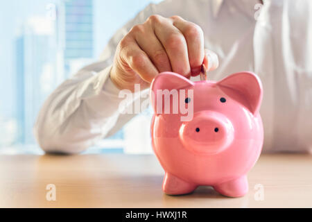 Mann, eine Münze in ein rosa Sparschwein-Konzept für Einsparungen und Finanzen Stockfoto