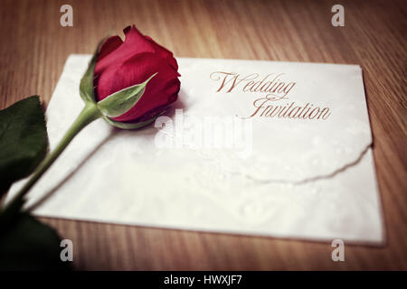 Hochzeitseinladung und rote Rose auf einem Holztisch Stockfoto
