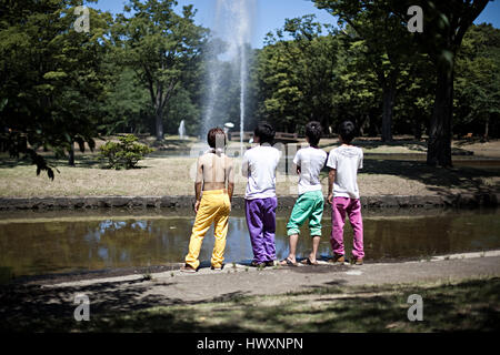 Vier japanische Jungs in bunten Hosen beobachten die Wasserfontäne im Yoyogi Park in Tokio, Japan. Stockfoto