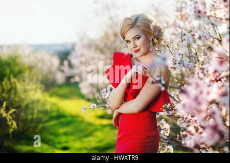 schöne junge Frau in einem roten Kleid in der Nähe von blühenden Frühling Baum Stockfoto