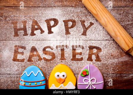 High-Angle Shot von einem Holztisch bestreut mit Puderzucker, Zucker oder Mehl, wo Sie den Text lesen Frohe Ostern, Cookies als verzierte Ostern dekoriert Stockfoto