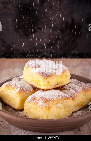 Vertikale Foto mit fünf Portionen an traditionellen hausgemachten Kuchen von süßen Quark gefüllt. Kuchen auf braunen Ton Platte gesetzt und fallenden Ei Stockfoto