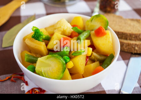 Gemüseeintopf (Kartoffeln, Spargel, Karotten, Rosenkohl, Mais, Erbsen, Wirsing, Brokkoli) in einer weißen Schale. Vegan. Stockfoto