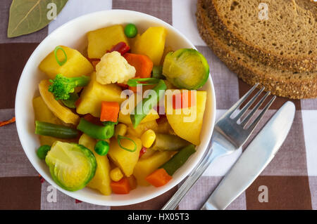 Gemüseeintopf (Kartoffeln, Spargel, Karotten, Rosenkohl, Mais, Erbsen, Wirsing, Brokkoli) in einer weißen Schale. Vegan. Stockfoto