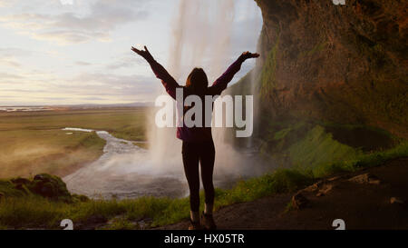 Hintere Ansicht Silhouette Frau mit ausgestreckten Armen hinter dem Wasserfall mit Blick auf abgelegenen Landschaft Stockfoto