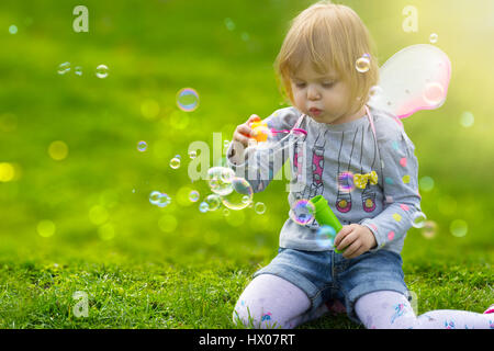 Kleinkind Mädchen mit Schmetterlingsflügeln Spaß im Park, Seifenblasen Stockfoto