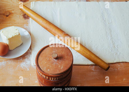 Block von frisch zubereiteten Teig auf einer bemehlten Arbeitsfläche mit einem hölzernen Nudelholz ausgerollt. Stockfoto