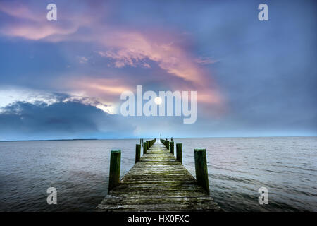 Full Moon rising über einen Chesapeake Bay Pier bei Sonnenuntergang mit Wolken Stockfoto