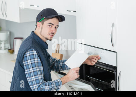 junge Handwerker in insgesamt Installation brandneue Ofen in der Küche Stockfoto