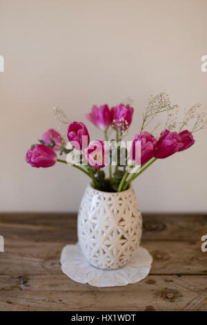 Bouquet von rosa Tulpen in weißer Vase platziert auf Seite machte Runde Serviette und rustikalen hölzernen Tischplatte Stockfoto