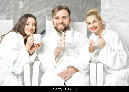 Freunde im Bademantel mit Teetassen in der Salzkammer sitzen entspannen. Anwendung von Salz-Therapie im Spa Stockfoto